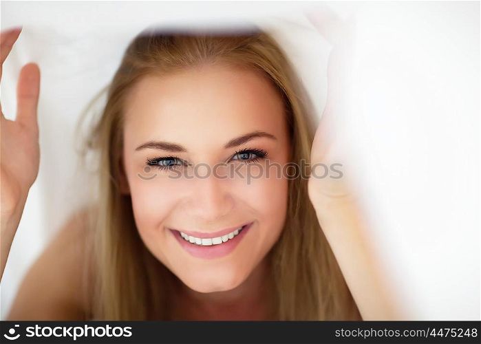 Closeup portrait of a nice cheerful female having fun in the bed, peeking out from under the sheets, spending happy time at home
