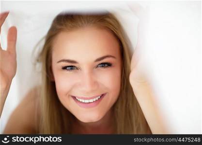 Closeup portrait of a nice cheerful female having fun in the bed, peeking out from under the sheets, spending happy time at home