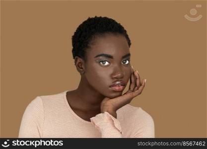 Closeup portrait of a sensual young black woman with short Afro hair, light makeup and lipstick posing by herself resting her head on the palm of her hand inside a studio with a pecan background.