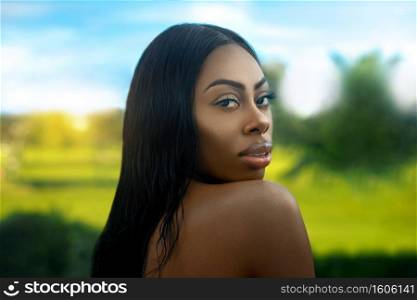 Closeup portrait of a sexy young black female"s face with beautiful makeup and luscious lips posing by herself in tropical surroundings.