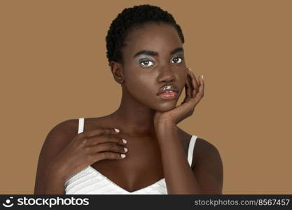 Closeup portrait of a sexy young black woman with short Afro hair, light makeup and lipstick posing by herself resting her head on the palm of her hand inside a studio with a pecan background.