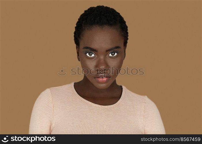 Closeup portrait of a young black woman with short Afro hair, light makeup and lipstick posing by herself inside a studio with a pecan background looking straight into the camera.
