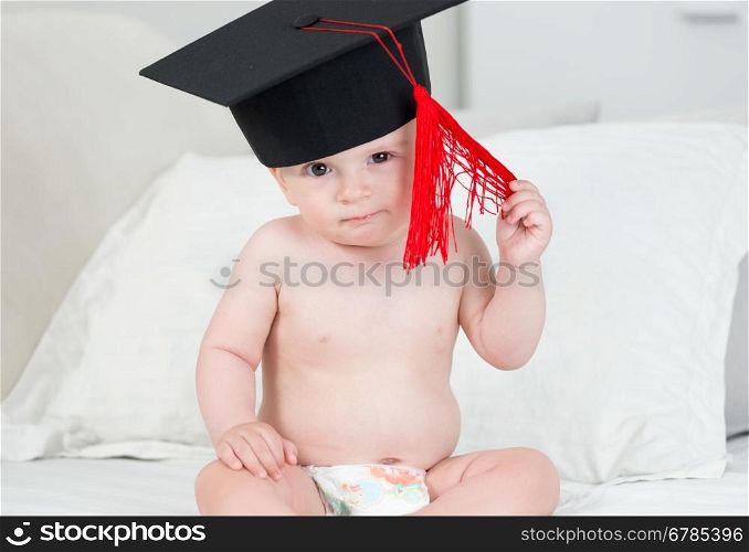 Closeup portrait of adorable baby boy in black graduation cap with red tassel