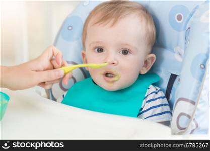 Closeup portrait of adorable baby in apron eating fruit sauce from spoon