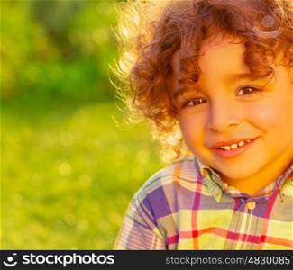 Closeup portrait of adorable sweet child on summer field, nice little boy with curly hair having fun on backyard, happiness and joy concept