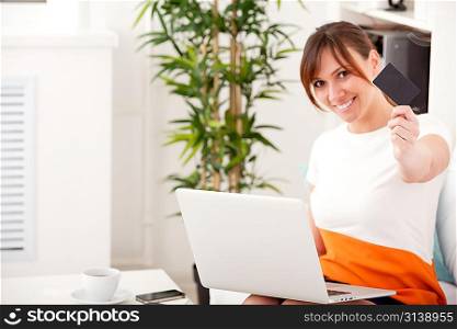 Closeup portrait of an attractive young woman with a laptop and card sitting on sofa at home
