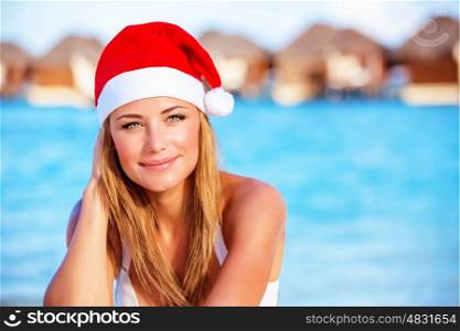 Closeup portrait of attractive blonde female wearing red Santa hat celebrating Christmas holidays on Maldives, exotic travel and vacation concept