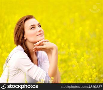 Closeup portrait of attractive brunette female sitting down on yellow floral field, rapeseed plantation, summer vacation concept