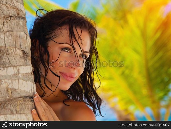 Closeup portrait of attractive brunette woman on exotic beach, hugging palm tree trunk, luxury tropical resort, summer vacation concept