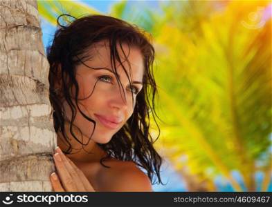 Closeup portrait of attractive brunette woman on exotic beach, hugging palm tree trunk, luxury tropical resort, summer vacation concept