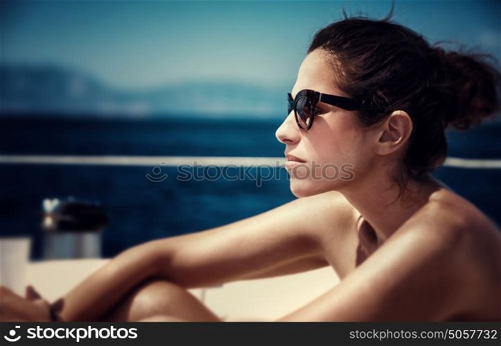 Closeup portrait of attractive female sitting on the yacht deck and enjoying warm sunny day, fashionable look, side view, sea cruise, traveling on luxury water transport