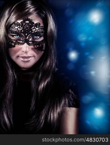 Closeup portrait of attractive female wearing black stylish mask on blue blur background, New Year masquerade, Christmas costume celebration