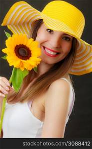Closeup portrait of attractive summer woman in yellow hat with sunflower in hand on black background