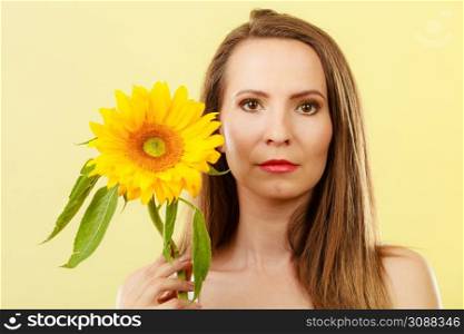 Closeup portrait of attractive woman with sunflower in her hand on yellow background