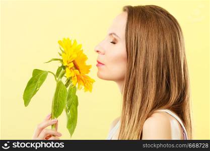 Closeup portrait of attractive woman with sunflower in her hand on yellow background, side view
