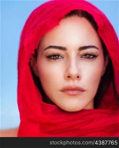 Closeup portrait of beautiful arabic woman wearing red headscarf over blue sky background, perfect natural makeup, traditional arabian beauty&#xA;