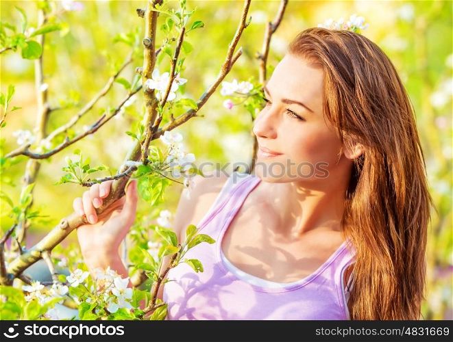 Closeup portrait of beautiful brunette female near blooming fruit tree, spring season, enjoying nature