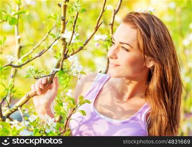 Closeup portrait of beautiful brunette female near blooming fruit tree, spring season, enjoying nature