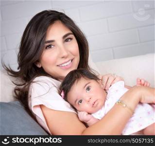 Closeup portrait of beautiful brunette mother with cute newborn daughter relaxing on sofa at home, happy young arabic family