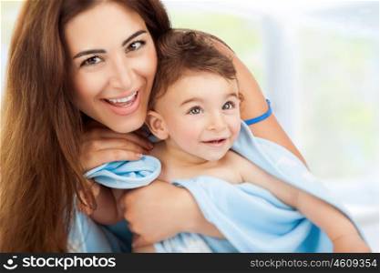 Closeup portrait of beautiful cheerful mother holding on hands cute little son after bath wrapped in towel, child's hygiene, happy healthy lifestyle