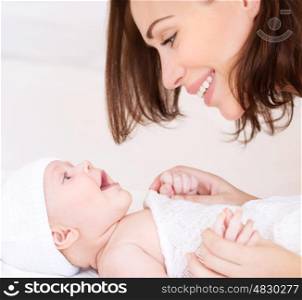 Closeup portrait of beautiful cheerful mother playing with cute little baby lying down on the bed, loving young family, happy motherhood concept