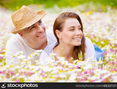 Closeup portrait of beautiful couple lying down on chamomile meadow and looking in one side, summer weekend, happiness and love concept