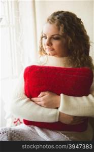 Closeup portrait of beautiful curly woman posing with red cushion at windowsill
