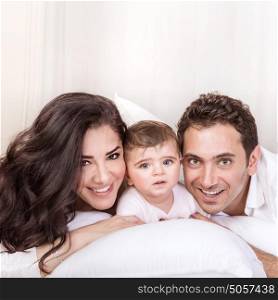Closeup portrait of beautiful parents with cute little baby having fun at home, lying down on the bed, happiness and family togetherness concept