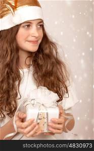 Closeup portrait of beautiful Santa girl holding in hands cute white gift box, wintertime holidays, looking in a side, Christmas joy, happiness concept