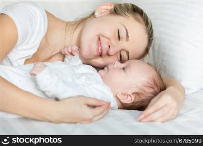 Closeup portrait of beautiful smiling woman lying with her cute baby on pillow at bed