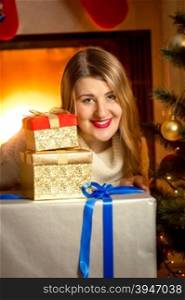 Closeup portrait of beautiful smiling woman posing with Christmas presents at fireplace