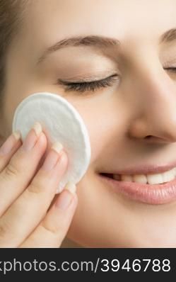 Closeup portrait of beautiful smiling woman removing makeup with cotton pad