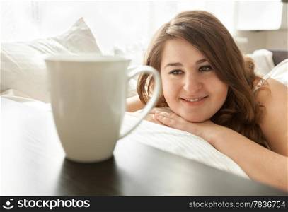 Closeup portrait of beautiful woman lying in bed and looking at cup