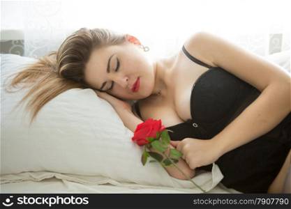 Closeup portrait of beautiful woman sleeping in bed and holding red rose