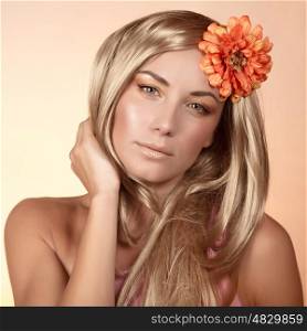 Closeup portrait of beautiful woman with orange flower in long blond hair isolated on beige background, gentle makeup, autumn season, spa salon, beauty concept