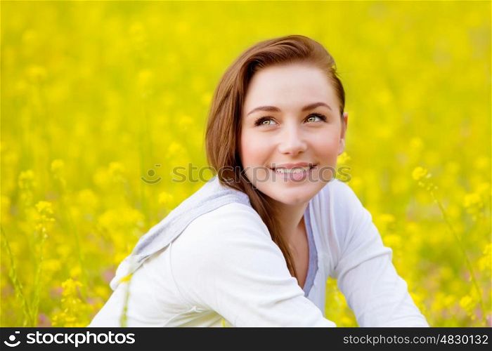 Closeup portrait of beautiful young female sitting down on fresh yellow floral field, coleseed meadow, summer vacation, relaxation outdoors