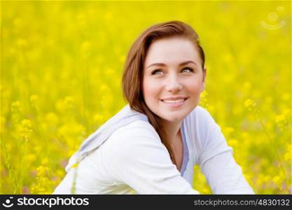 Closeup portrait of beautiful young female sitting down on fresh yellow floral field, coleseed meadow, summer vacation, relaxation outdoors