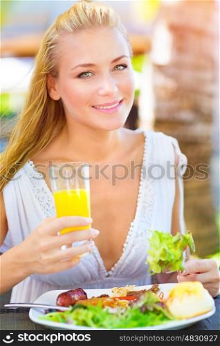 Closeup portrait of beautiful young happy female having lunch outdoors, drink refreshing orange juice and eating green salad, healthy eating concept