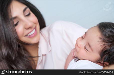 Closeup portrait of beautiful young happy mother having fun with her little newborn baby at home, enjoying first day of motherhood, love and happiness concept