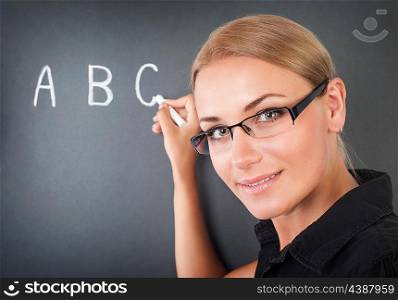 Closeup portrait of beautiful young teacher writing on blackboard letters, cute educator in elementary school, start of educational season&#xA;