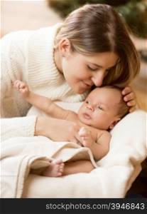 Closeup portrait of caring mother kissing baby boy son lying on white blanket in basket