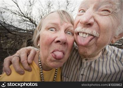 Closeup portrait of crazy elderly couple outdoors sticking out tongues