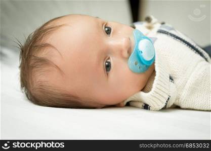 Closeup portrait of cute 1 months old baby boy with soother lying on bed