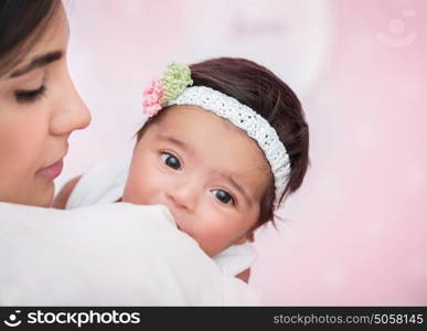 Closeup portrait of cute adorable little baby girl peeking over his shoulder mother, wearing nice head accessory, happy young family concept