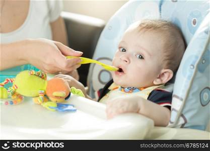 Closeup portrait of cute adorably baby boy sitting in chair and eating from spoon