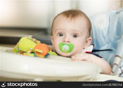Closeup portrait of cute baby boy with soother waiting for breakfast in highchair