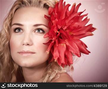 Closeup portrait of cute blond girl with big red flower in head isolated on pink background, natural makeup, spa concept