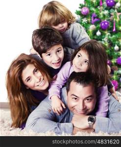 Closeup portrait of cute cheerful family lying down near Christmas tree at home, happy parents with three kids celebrate New Year holiday, love concept