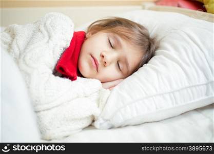 Closeup portrait of cute girl in sweater and scarf lying on white pillow