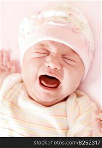 Closeup portrait of cute little baby girl crying in pink pajama &amp; hat?
